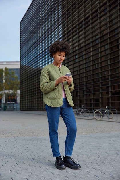세련된 옷을 입은 소녀는 현대적인 스마트폰 가제트를 들고 도시 환경에서 경로 다운로드 탐색 응용 프로그램을 찾으려고 합니다.