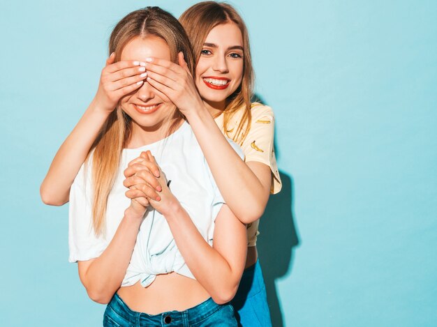 Girl surprising her female best friend. Model covering her eyes and hugging  from behind. 