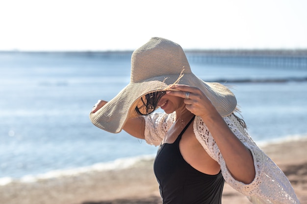 The girl in a swimsuit covered her face with a large hat. Summer vacation concept at sea.