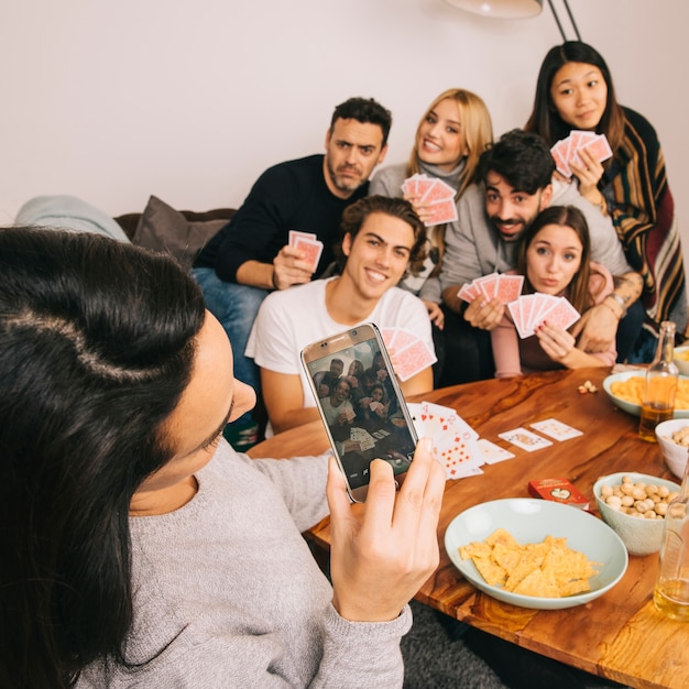 Girl taking photo of friends playing cards game