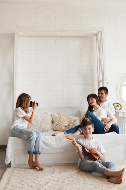 Girl taking photo of her parents and her brother playing ukulele at home