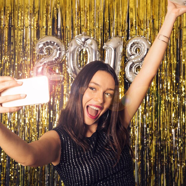 새 해 축하에 빛나는 스마트 폰으로 selfie를 복용하는 여자