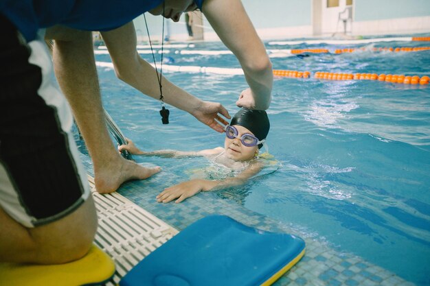 Girl taking swiming lesson. Male coach or dad helping to her with goggles, while swimming.