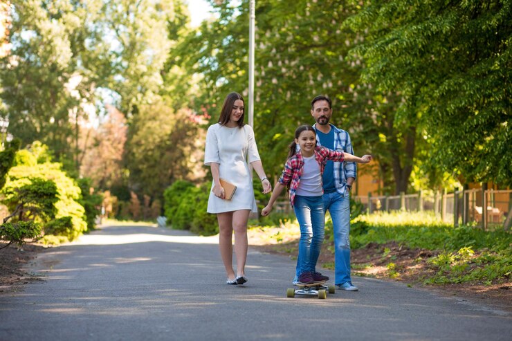 मुफ़्त फोटो girl teenager riding a skateboard in the city park. parents watching her and smiling