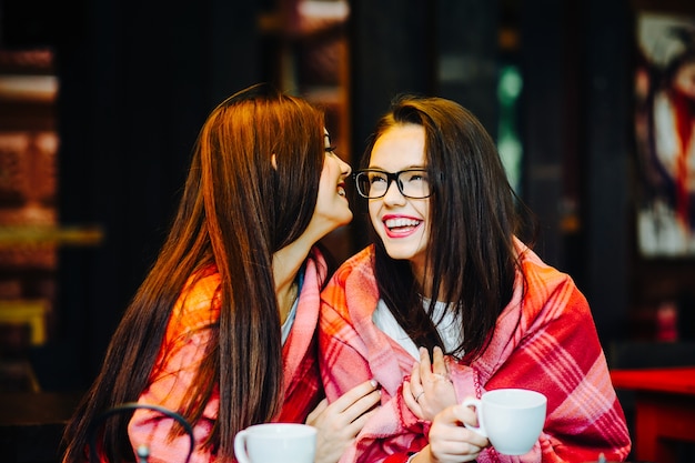 Girl telling a secret to another girl covered a blanket