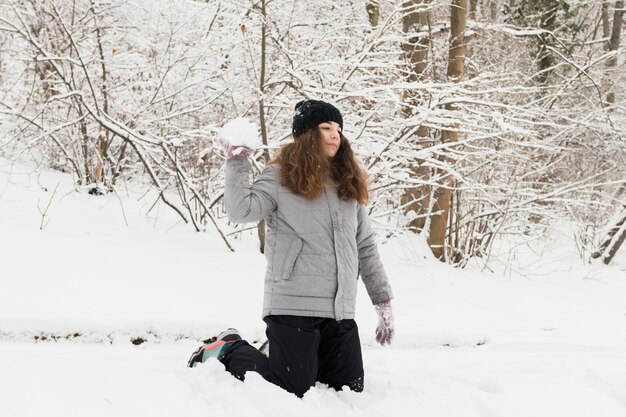 Ragazza che getta la palla di neve nella foresta di inverno