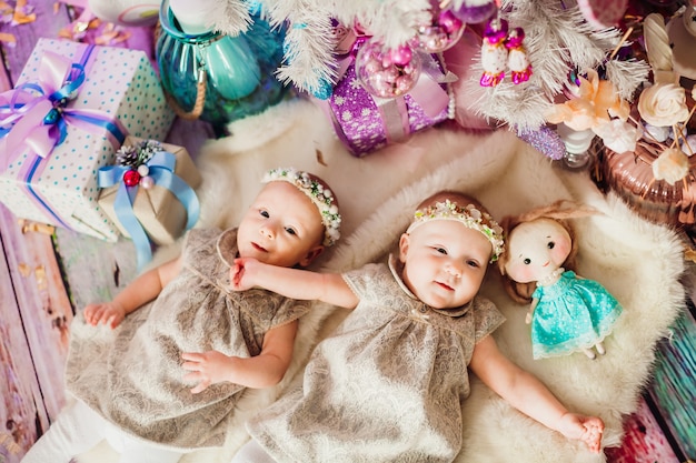 Girl-twins lie under pink Christmas tree 