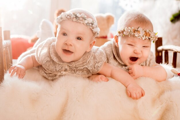 Girl-twins in wreathes and dresses lie on a bed in the rays of morning sun 