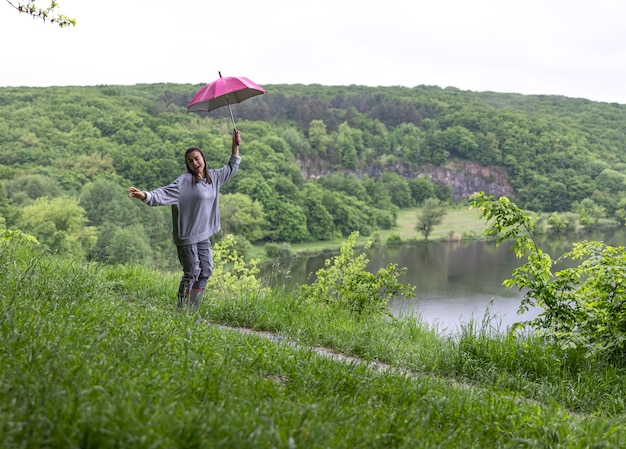 Girl Jumping under an Umbrella Near a Lake in Rainy Weather