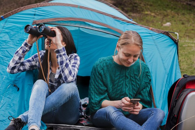 Girl using her binoculars next to her friend with her mobile phone