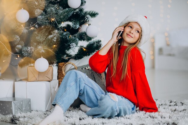 Girl using phone by christmas tree on christmas