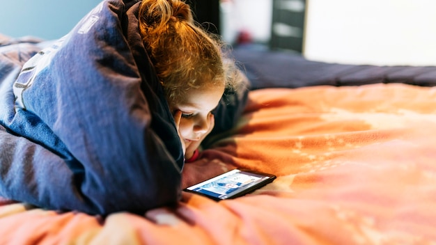 Девушка с помощью смартфона под одеялом
