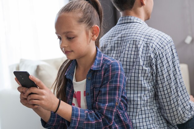 Girl using smartphone near brother