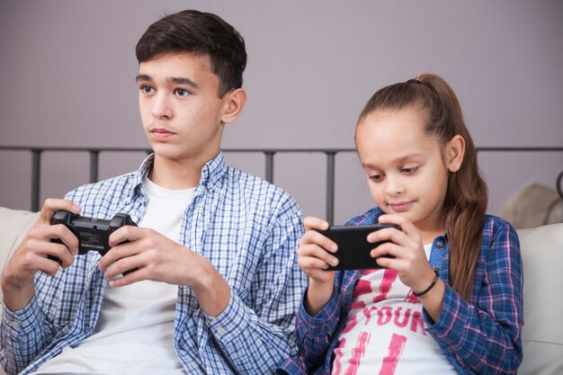 Girl using smartphone near teenager with controller