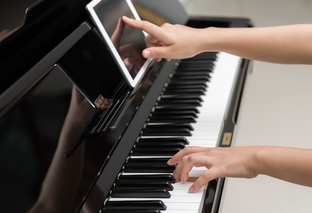 Девушка с помощью планшета, чтобы научиться играть на пианино