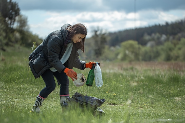 Girl volunteer collects garbage in the forest, takes care of the environment.