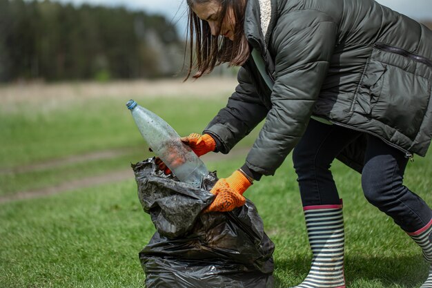 Girl volunteer collects garbage in the forest, takes care of the environment.