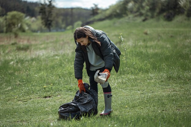 Girl volunteer collects garbage in the forest, takes care of the environment