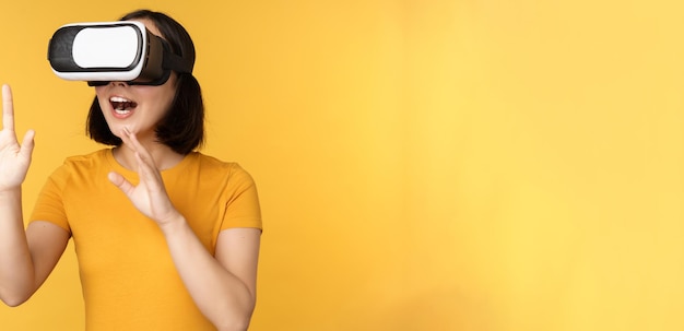 Девушка в VR Красивая молодая азиатка в очках виртуальной реальности и играет в чате, практически стоя на желтом фоне
