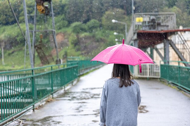 A girl walks under an umbrella in rainy weather on a bridge in the forest.