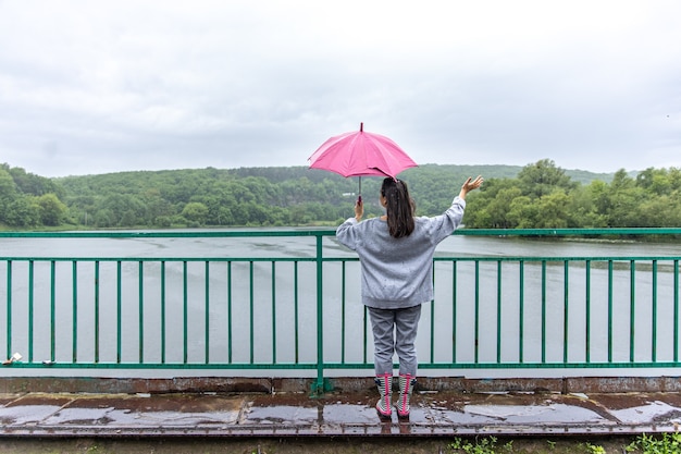 A girl walks under an umbrella in rainy weather on a bridge in the forest.