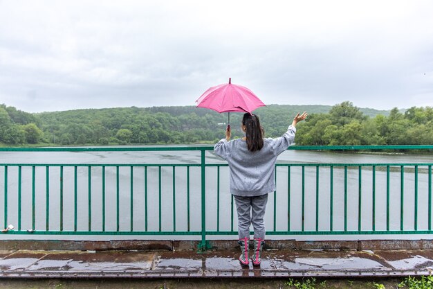 雨の日に傘をさして森の橋を歩く女の子。