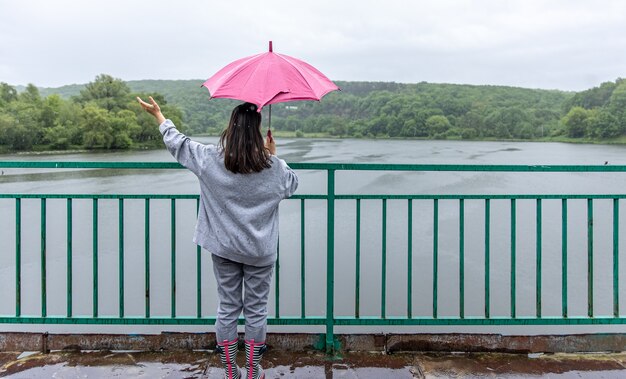 A girl walks under an umbrella in rainy weather on a bridge in the forest.