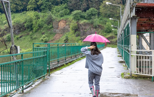 A girl walks under an umbrella in rainy weather on a bridge in the forest