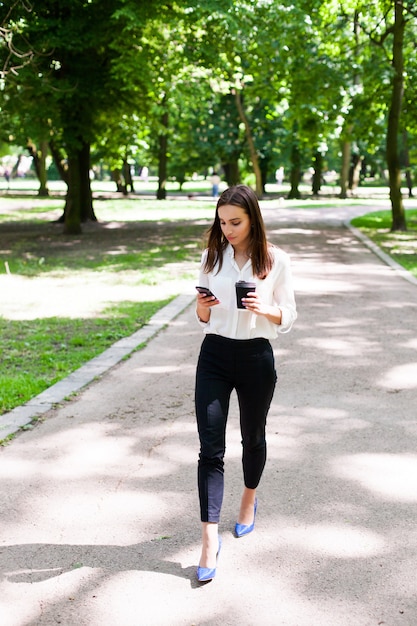 소녀는 그녀의 손에 전화와 공원에서 커피 한잔과 함께 산책