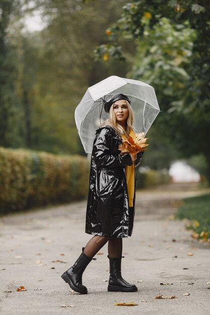 女の子が歩きます。黒いコートを着た女性。黒い帽子をかぶった金髪。傘を持つ女性。