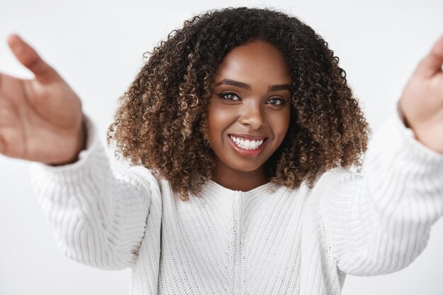 Girl wanna warm hugs Tender and cute africanamerican female in sweater extending hands towards camera to cuddle and welcome friend smiling delighted with gentle gaze over white background