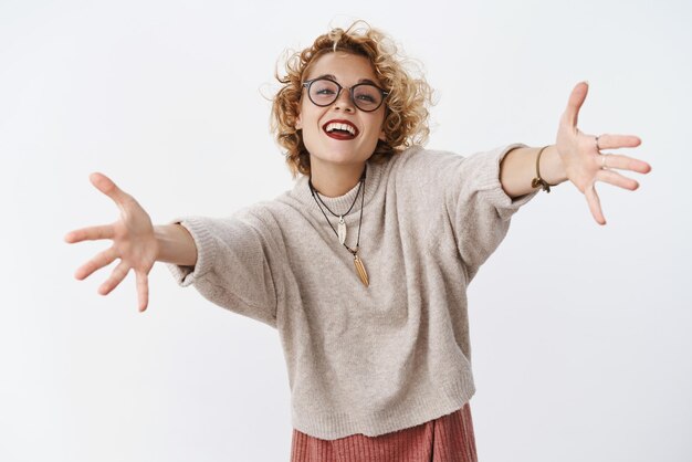 Girl wants hugs Portrait of charming happy and enthusiastic attractive european female with short blond hair in glasses and sweater stretch hands to camera for cuddles and smiling friendly welcoming