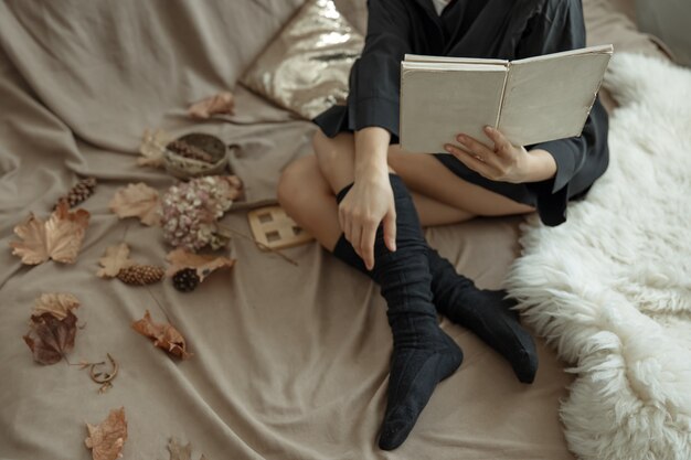 따뜻한 스타킹을 입은 소녀가 침대에 누워 아늑한 가을 배경인 책을 읽습니다.