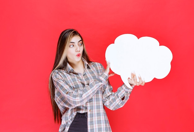 Free photo girl in warm sweater holding a cloud shape ideaboard and looks surprized