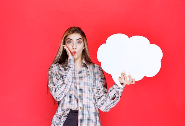 Free photo girl in warm sweater holding a cloud shape ideaboard and looks surprized