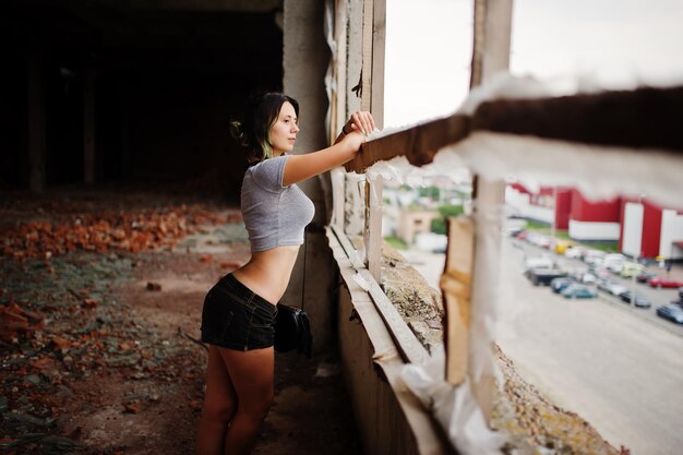 レンガの壁のある廃墟のファクトリーでショートパンツを着ている女の子