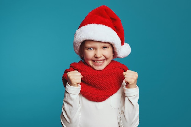 Девушка в рождественской шапке и красном шарфе поднимает кулаки и празднует