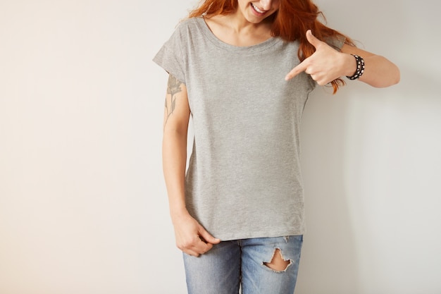 Girl wearing grey blank t-shirt standing on white wall