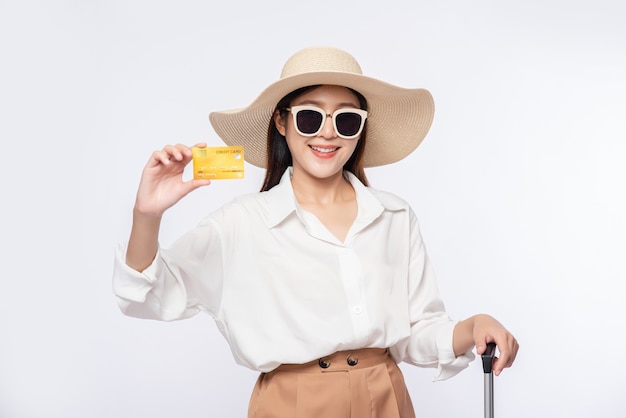 Девушка в шляпе держит кредитную карту и чемодан для путешествия