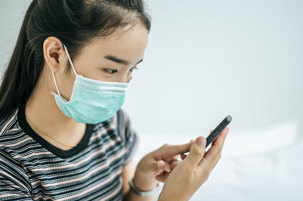 A girl wearing a mask and a striped shirt playing a smartphone.