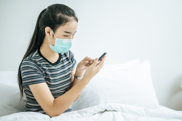 A girl wearing a mask and a striped shirt playing a smartphone.