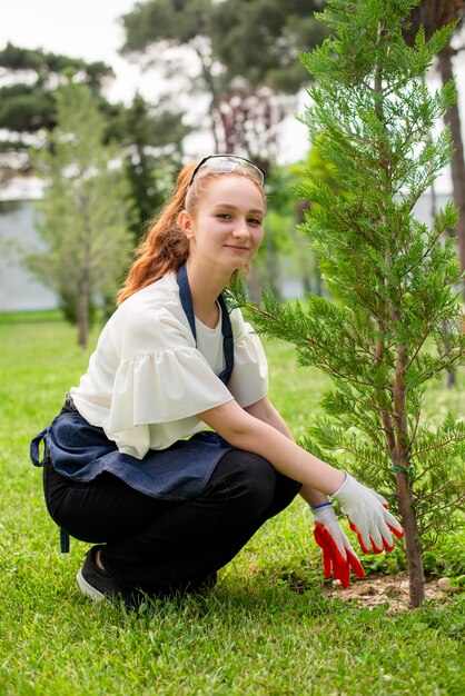 Девушка в комбинезоне и перчатках выращивает деревья в саду
