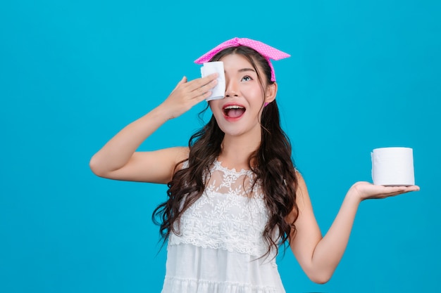 Girl wearing white pajamas Using tissue paper on her face on a blue .