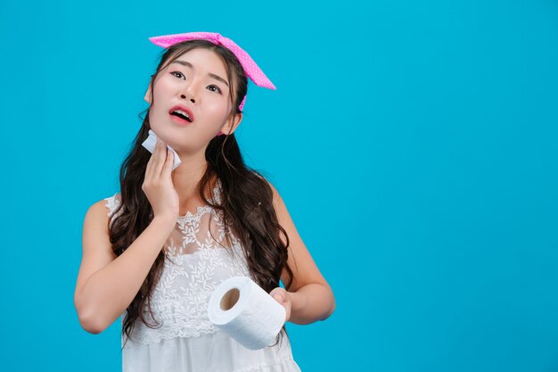 Girl wearing white pajamas Using tissue paper on her face on a blue .