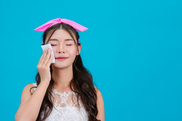 Girl wearing white pajamas Using tissue paper on her face on a blue .