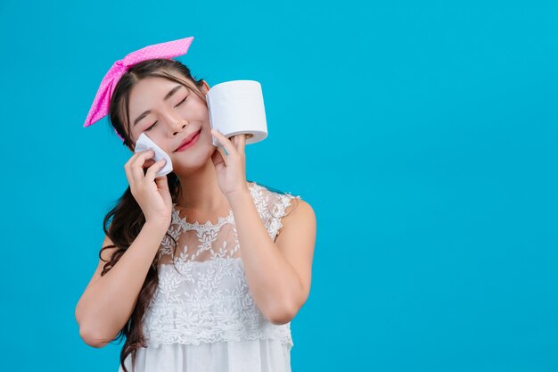 Girl wearing white pajamas Using tissue paper on her face on a blue .