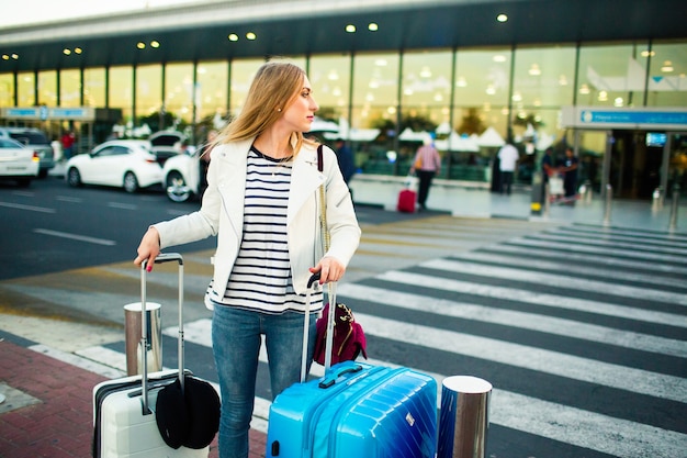 Girl in white jacket stands on crossing with blue and white suitcases