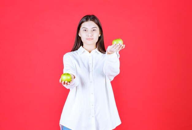 녹색 사과를 손에 들고 고객에게 제공하는 흰 셔츠를 입은 소녀