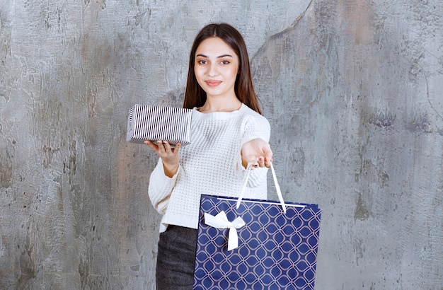 Girl in white shirt holding a silver gift box and a blue shopping bag.