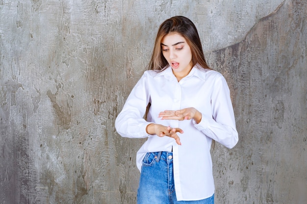 Girl in white shirt standing on a concrete wall and checking time.